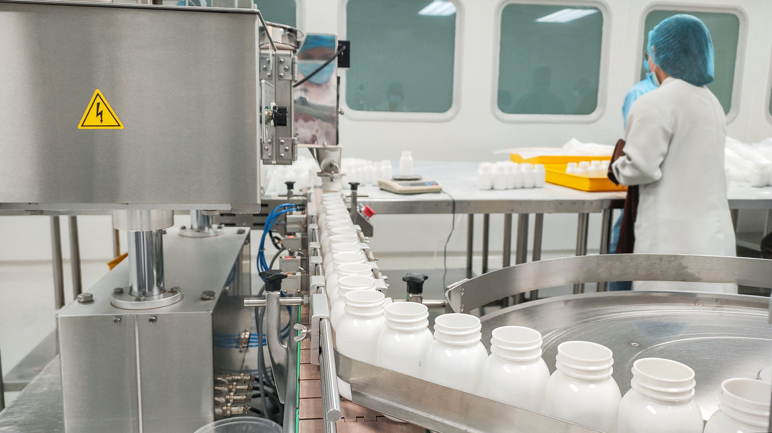 A professional in protective gear oversees a conveyor belt of finished medical bottles in a modern production department
